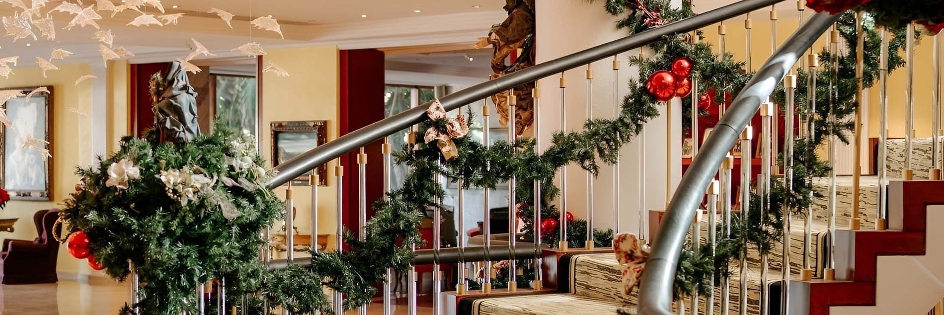 Una escalera elegantemente decorada con guirnaldas navideñas, adornos rojos y lazos es el foco central de este interior festivo.