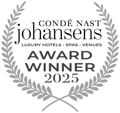 En silvergrå lagerkrans inramar texten "CONDÉ NAST JOHANSENS LUXURY HOTELS - SPAS - VENUES AWARD WINNER 2025" på en svart bakgrund.