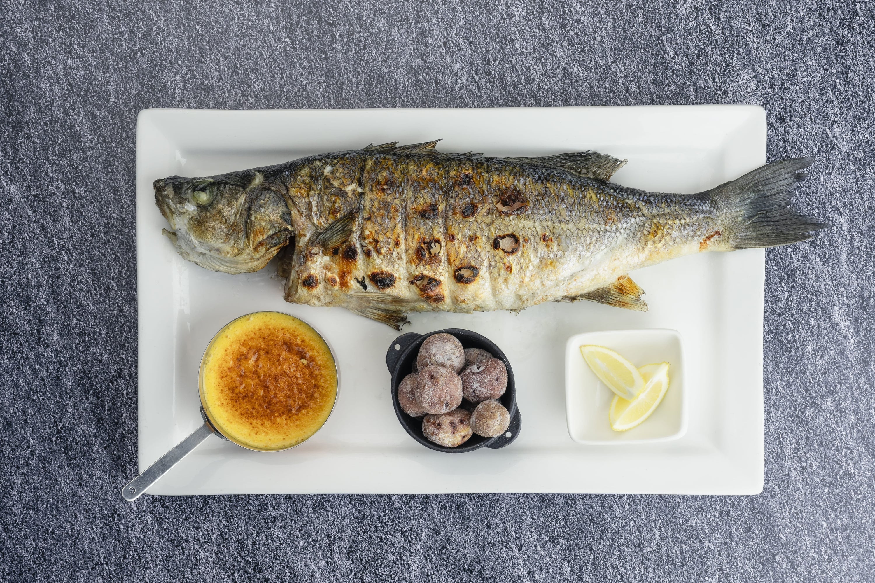 Una sala ristorante elegante e accogliente è arredata con numerosi tavoli apparecchiati, sedie rosse e caratteristiche lampade a sospensione in legno pendenti da un soffitto con travi a vista.