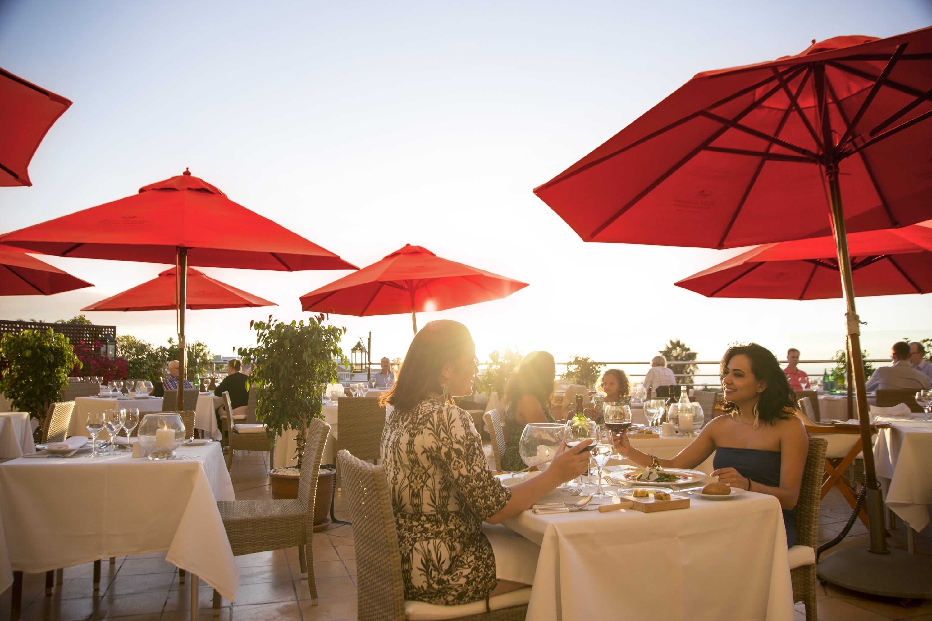 En fiskrätt med en bit fisk med skinnet kvar, grönsaker och en krämig sås serveras på en vit tallrik på en vit duk mot en mörk bakgrund.