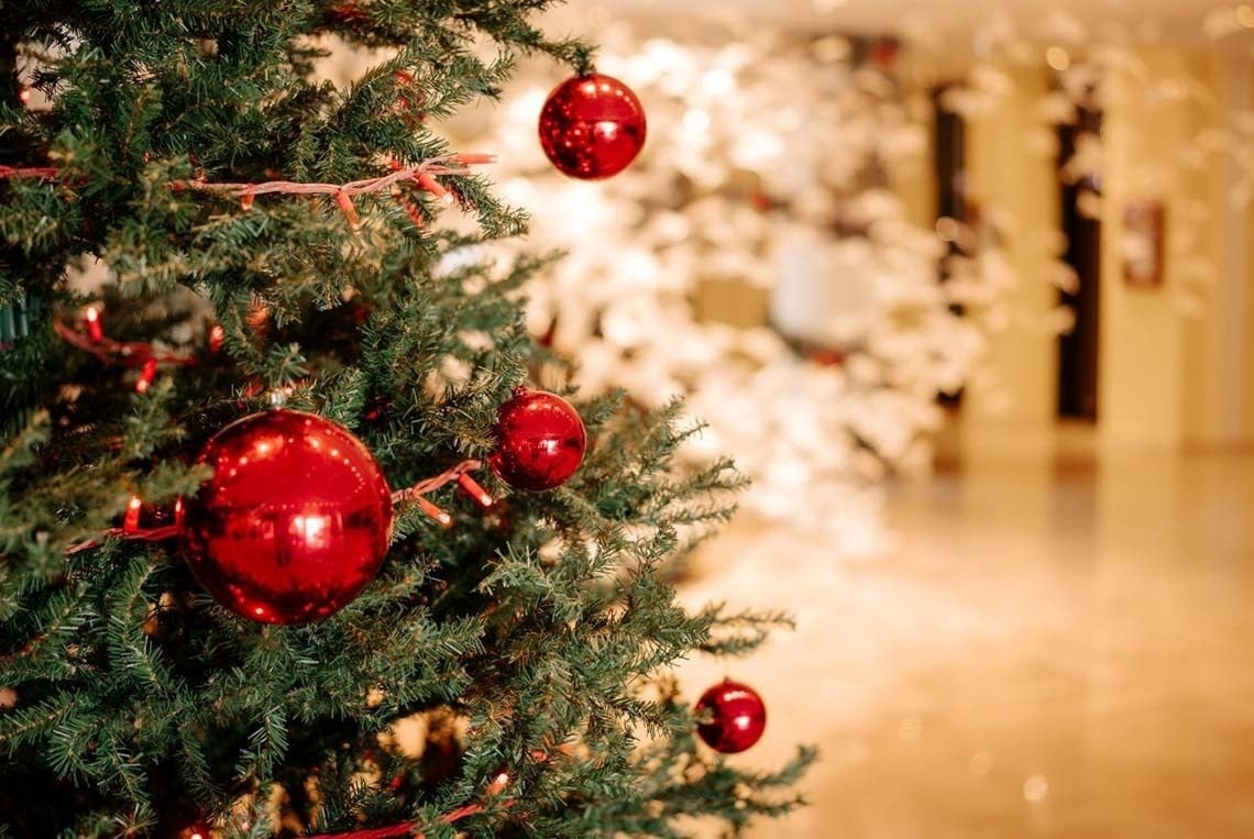 Dos copas de champán burbujeante celebran la Navidad junto a un árbol decorado con adornos y serpentinas doradas, bajo una lluvia de chispas brillantes.