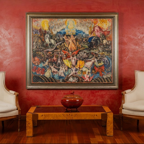 Una stanza riccamente decorata presenta un grande dipinto dettagliato su una vivace parete rossa, affiancato da due classiche poltrone imbottite e un tavolino da caffè in legno.