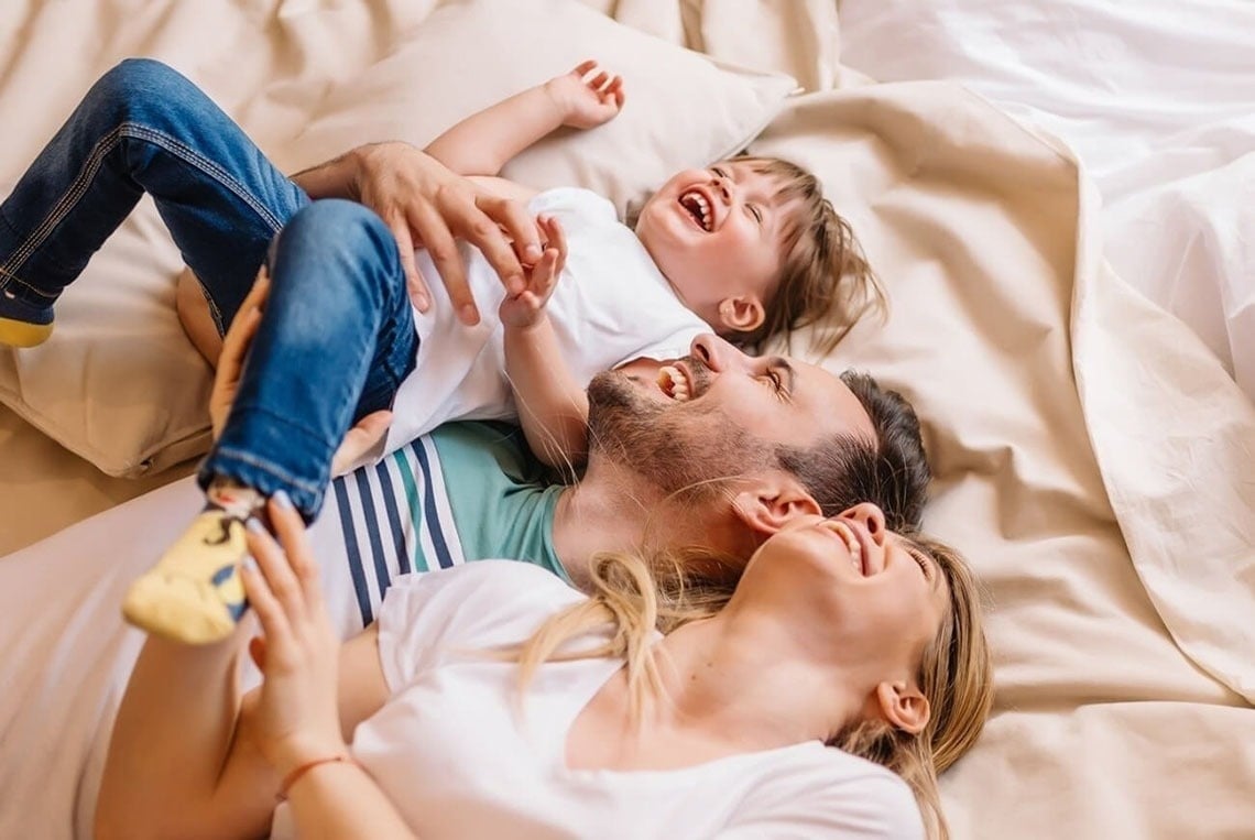 un hombre , una mujer y un niño están acostados en una cama y riendo