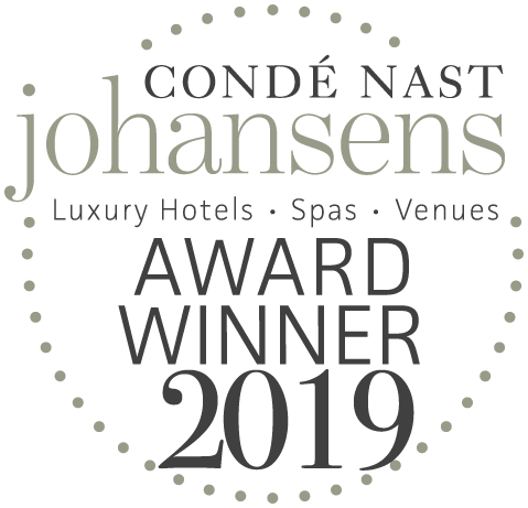 En gråskalelogotyp med texten "Condé Nast Johansens Award Winner 2019" för lyxhotell, spa och mötesplatser, inramad av en prickad cirkel.