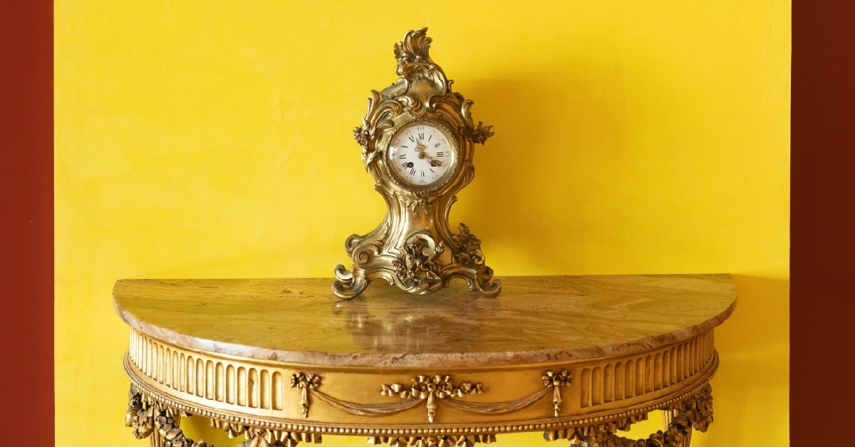 Una sala de comedor formal presenta una gran mesa redonda elegantemente puesta con numerosas sillas rojas, plantas y un cuadro en la pared.