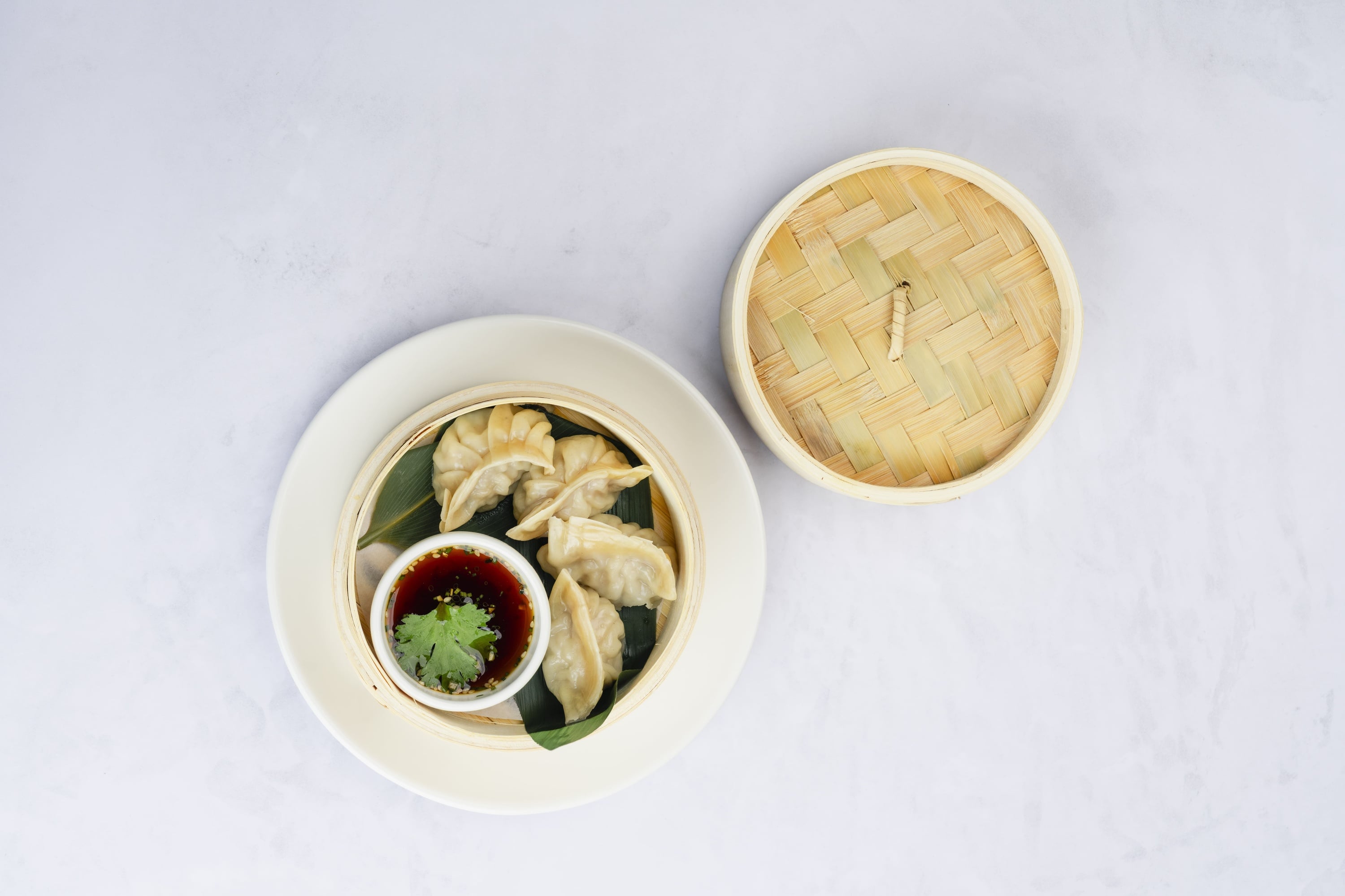 Una sonriente chef asiática con uniforme rojo y gorro negro posa con los brazos cruzados en un ambiente de restaurante.