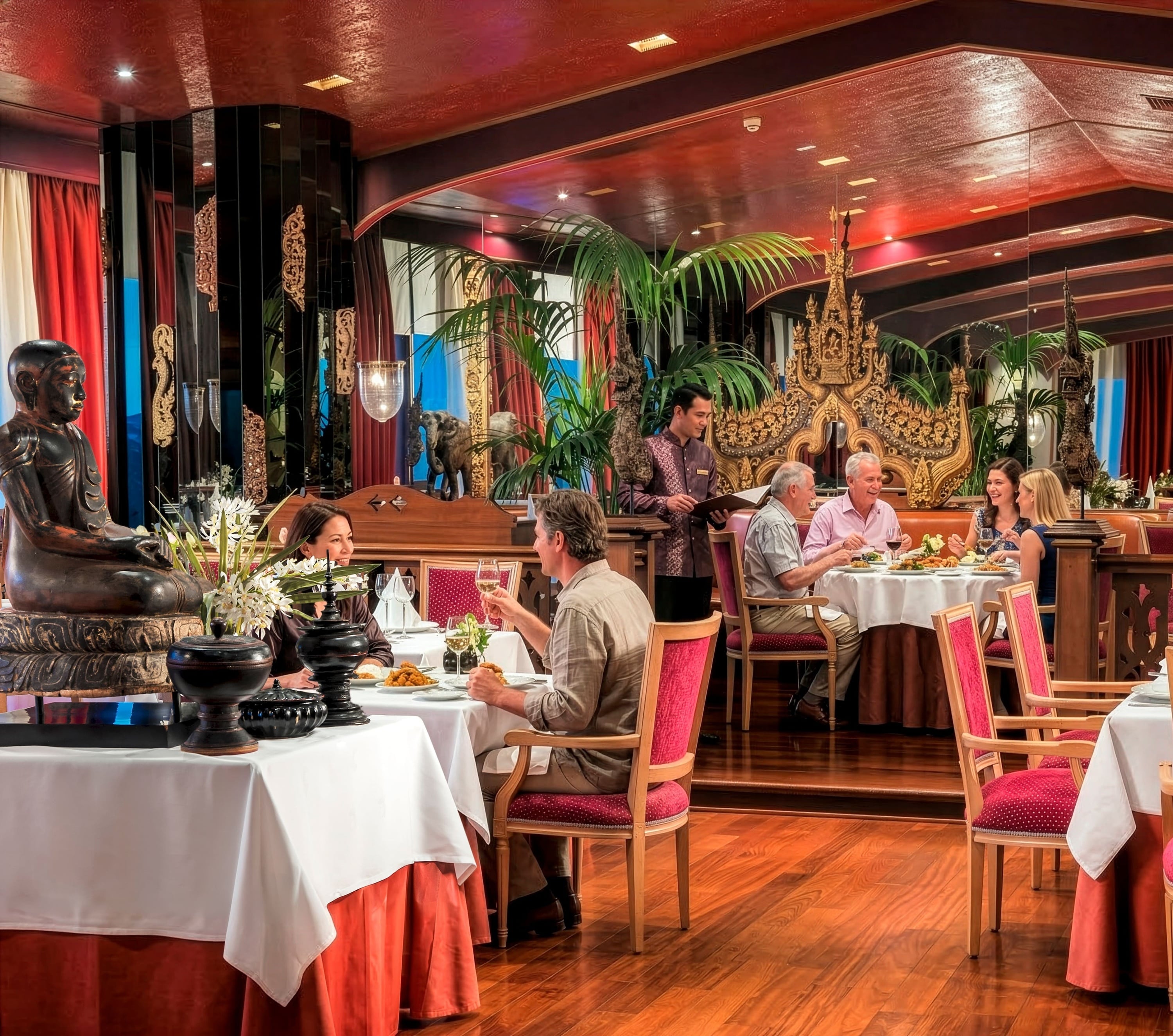 Un lujoso restaurante de inspiración asiática con intrincadas decoraciones doradas y una estatua de Buda, donde varios comensales disfrutan de una comida mientras son atendidos por un camarero.