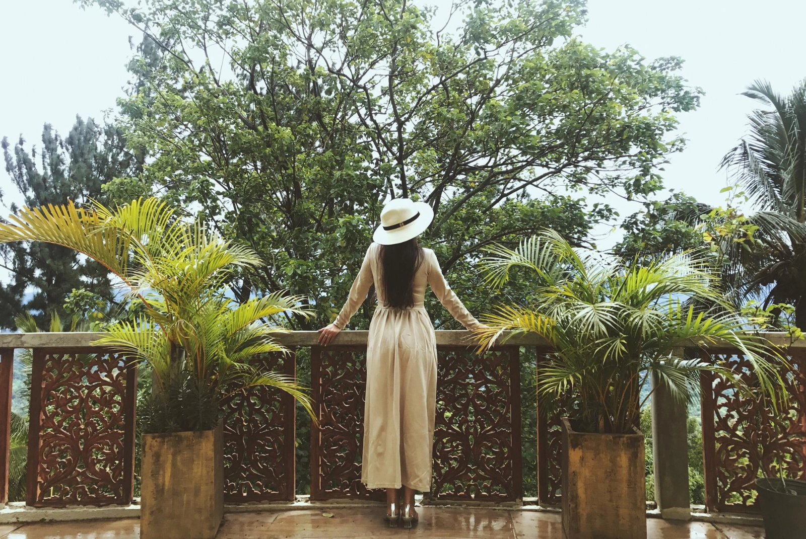 una mujer con un sombrero se sienta en un balcón mirando a los árboles