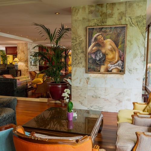 Un elegante salone lussuosamente arredato con marmo, varie sedute, un quadro e ampie vetrate su un giardino lussureggiante.