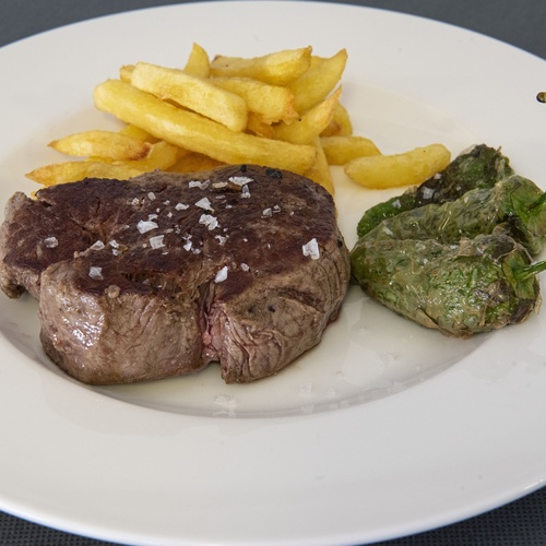 un plato blanco con carne y papas fritas y un pimiento verde