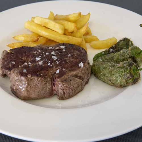 un plato blanco con carne y papas fritas y un pimiento verde