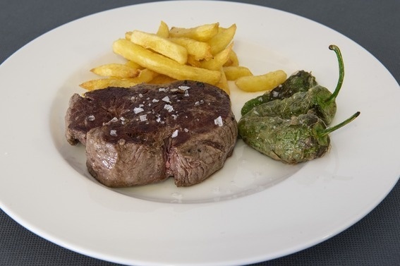 un plato blanco con carne y papas fritas y un pimiento verde