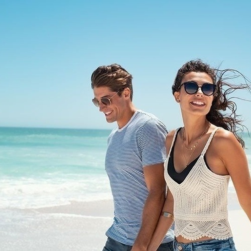 a man and woman wearing sunglasses are walking on the beach
