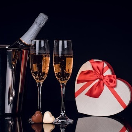 eine Flasche Champagner in einem Eiskübel neben zwei Sektgläsern und einer herzförmigen Geschenkbox