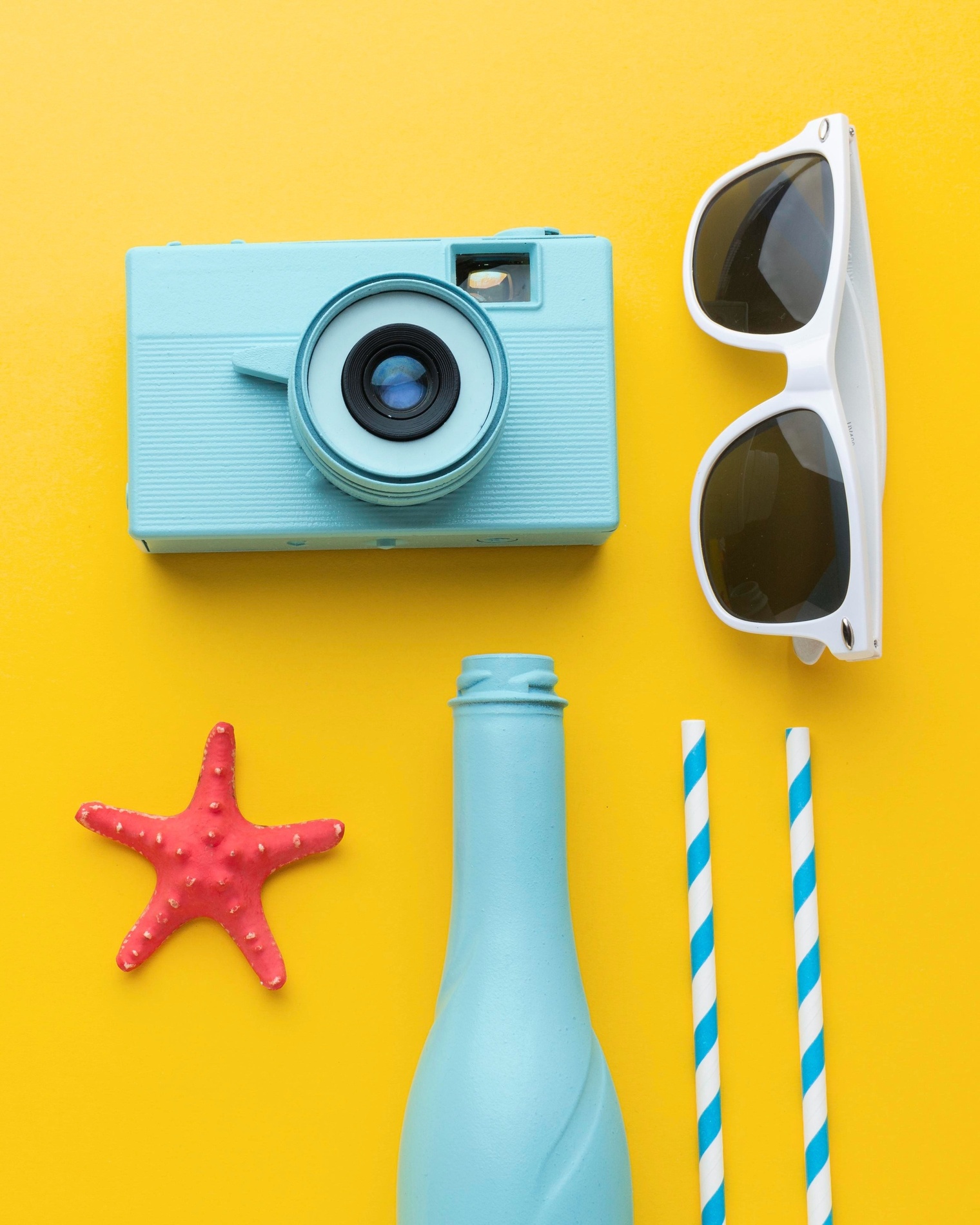 una cámara , gafas de sol , una botella y una estrella de mar sobre un fondo amarillo