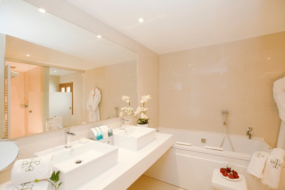 La imagen muestra un baño moderno y elegante con doble lavabo, una bañera y detalles decorativos como orquídeas y fresas, creando un ambiente de lujo y confort.