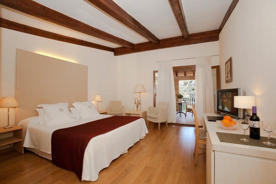 Un dormitorio luminoso con vigas de madera en el techo, cama grande, suelo de madera y acceso a un balcón.