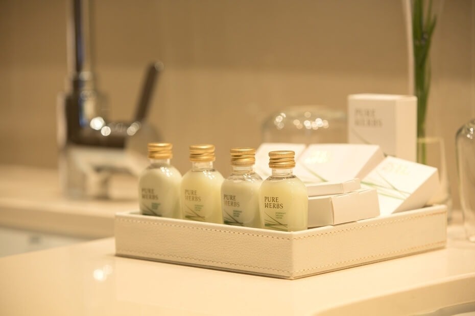 En un baño, una bandeja clara exhibe cuatro pequeñas botellas de artículos de tocador "Pure Herbs" junto a otros productos de higiene personal.