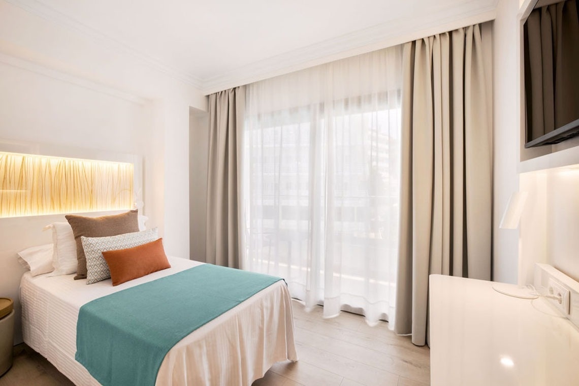 una habitación con una cama y una ventana con cortinas blancas
