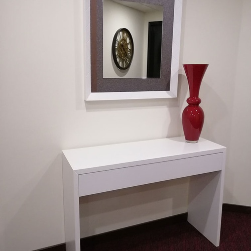 Consola blanca con jarrón rojo y espejo decorativo en Hotel Monaco.
