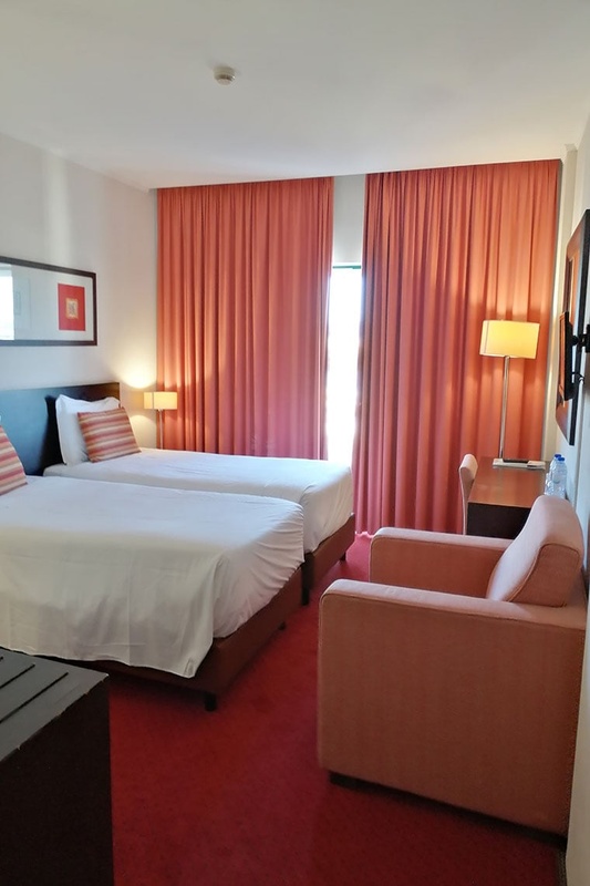 Cama de casal com travesseiros decorativos no Hotel Monaco, com mesas de cabeceira e iluminação moderna.