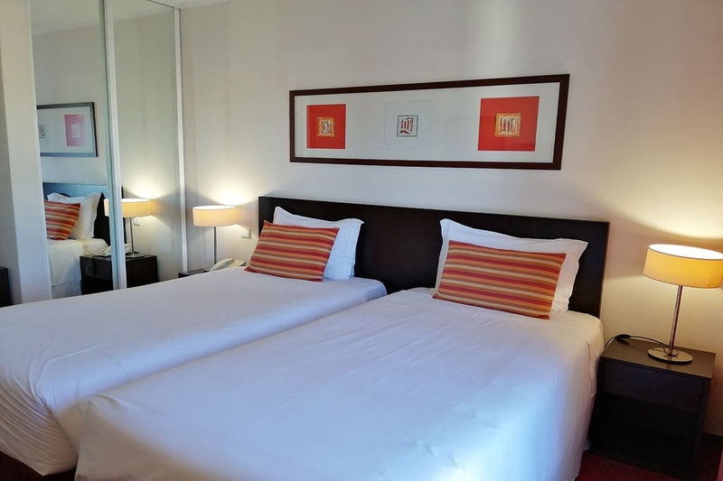 Cama de casal com travesseiros decorativos no Hotel Monaco, com mesas de cabeceira e iluminação moderna.