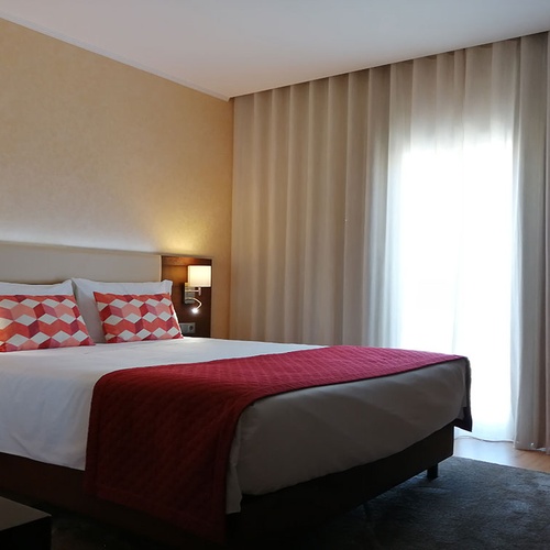 Cómoda cama en habitación de Hotel Monaco con mantas rojas y cojines decorativos.