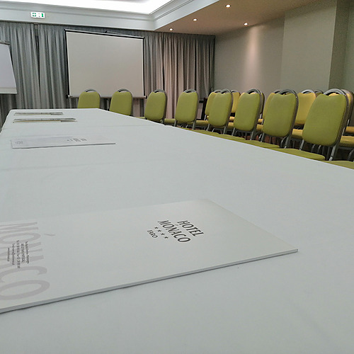 Sala de reuniões com mesa coberta, cadeiras amarelas e projetor. Hotel Monaco.