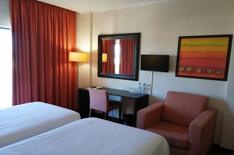 Cama de casal com travesseiros decorativos no Hotel Monaco, com mesas de cabeceira e iluminação moderna.