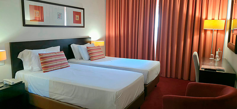 Cama de casal com travesseiros decorativos no Hotel Monaco, com mesas de cabeceira e iluminação moderna.