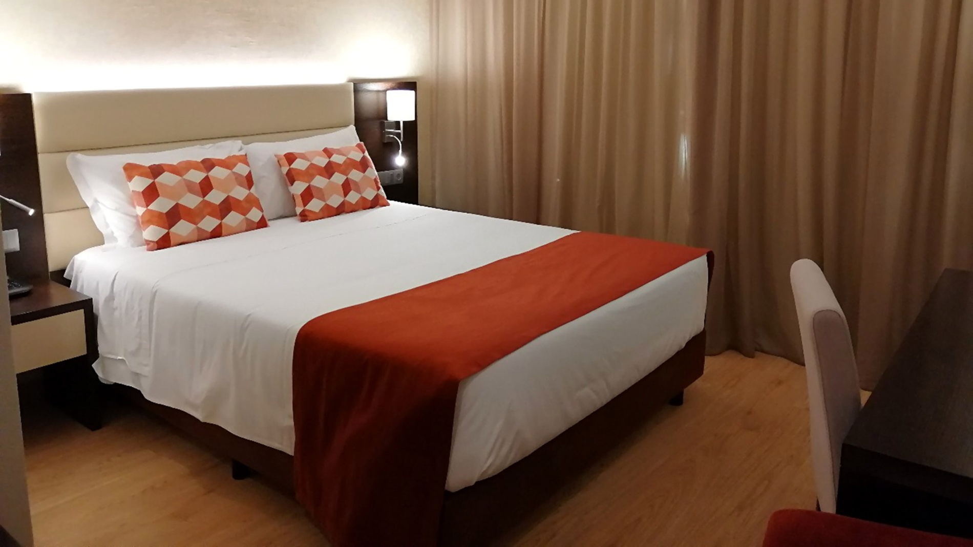 Quarto elegante com cama de casal, travesseiros decorados e piso de madeira no Hotel Monaco.