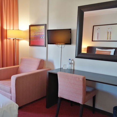 Habitación con sillón rosa, escritorio y espejo en Hotel Monaco.