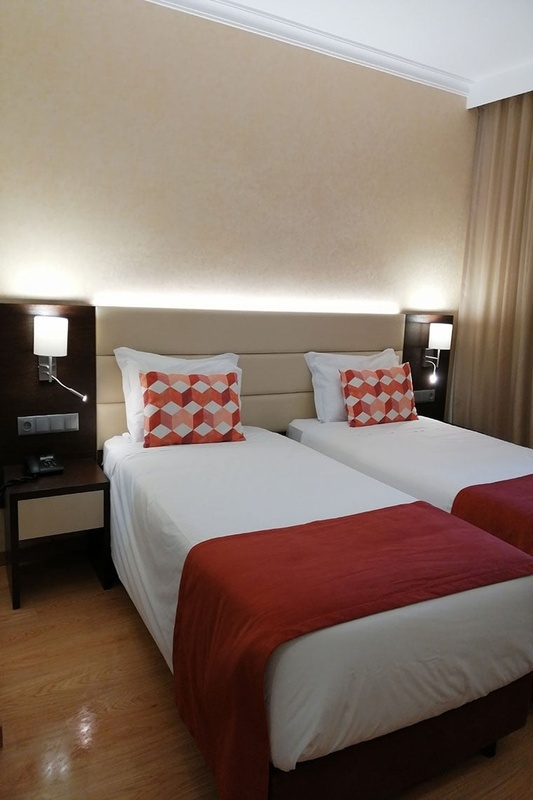 Cama de casal com travesseiros decorativos no Hotel Monaco, com mesas de cabeceira e iluminação moderna.