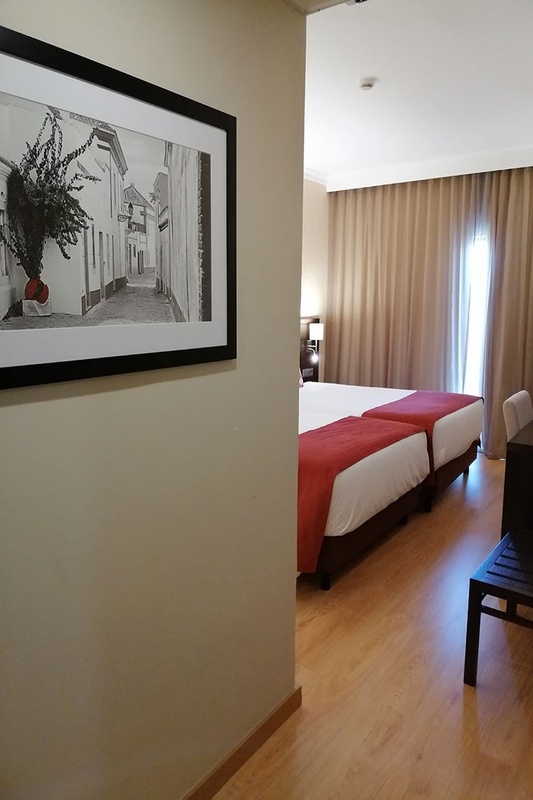 Cama de casal com travesseiros decorativos no Hotel Monaco, com mesas de cabeceira e iluminação moderna.