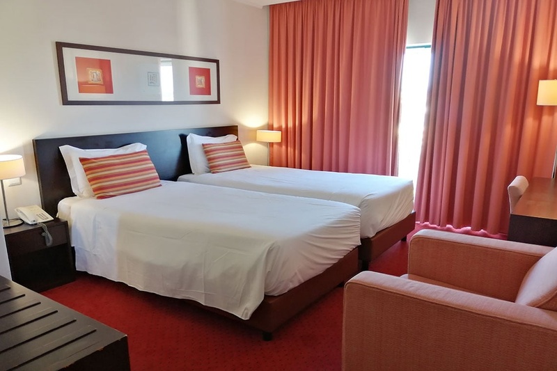 Cama de casal com travesseiros decorativos no Hotel Monaco, com mesas de cabeceira e iluminação moderna.