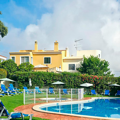 Piscina em hotel Hotel Monaco, com espreguiçadeiras azuis e casas amarelas ao fundo.