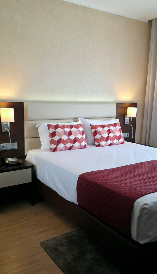 Cama confortável com almofadas decorativas e cobertor bordô em um quarto de hotel. Hotel Monaco