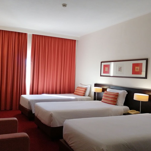 Habitación triple en Hotel Monaco con cortinas naranjas y camas cómodas.