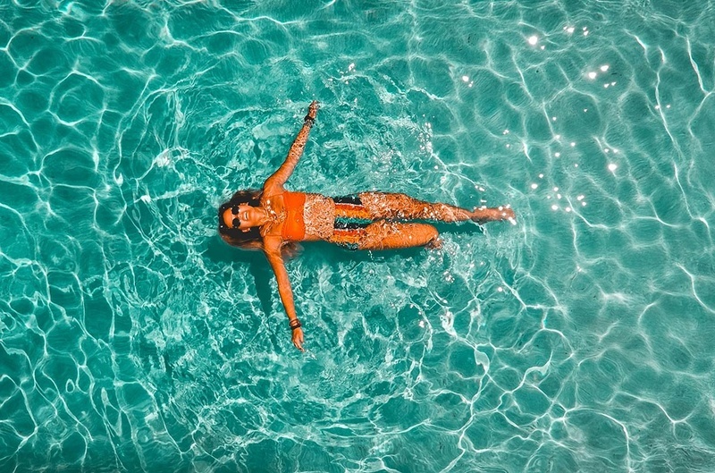 Mulher relaxa na piscina do Hotel Monaco com água cristalina e sol.