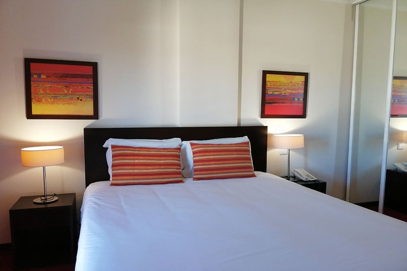 Quarto aconchegante no Hotel Monaco com cama de casal, travesseiros decorativos e cortinas elegantes.