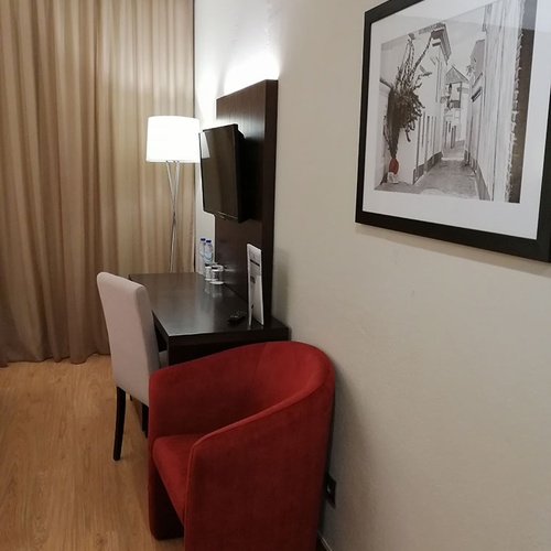 Elegante escritorio de Hotel Monaco con sillón rojo, TV y lámpara de pie.