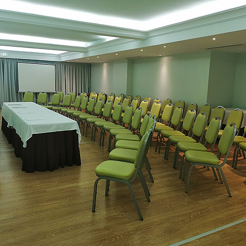 Sala de conferências com cadeiras verdes e uma mesa longa, ideal para eventos e reuniões. Hotel Monaco