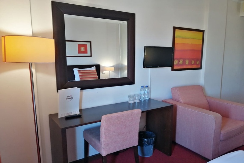 Cama de casal com travesseiros decorativos no Hotel Monaco, com mesas de cabeceira e iluminação moderna.
