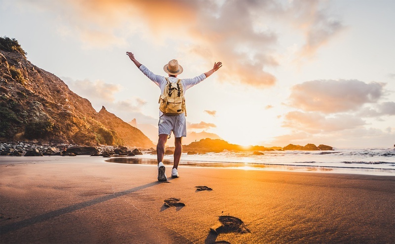 un hombre con una mochila camina por la playa al atardecer