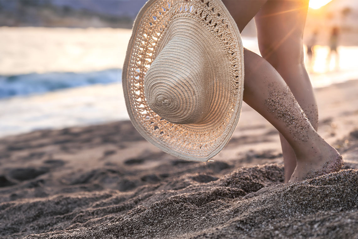Woman's legs with sand at the beach near the ocean, holding a straw hat <p>	<strong>Hotel Nerja Club by Dorobe</strong></p>.