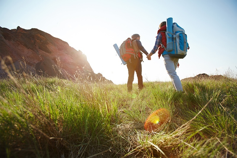 two people with backpacks are walking through a grassy field