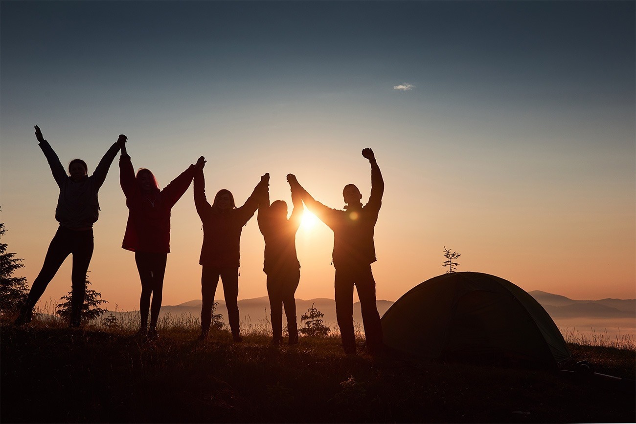 un grupo de personas sostiene sus manos en el aire frente a una carpa al atardecer