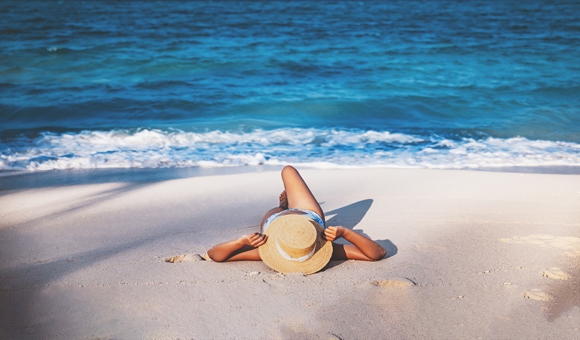 a woman in a straw hat is laying on the beach