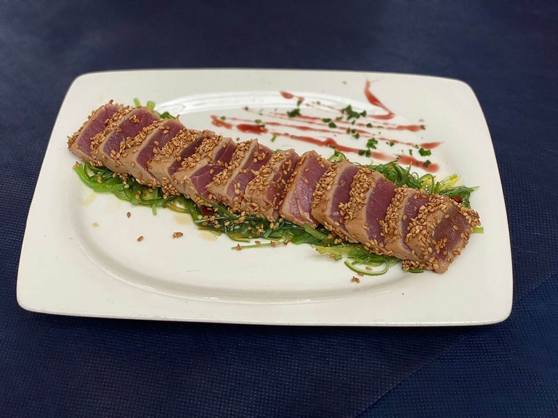 un plato blanco con un trozo de atún y semillas de sésamo