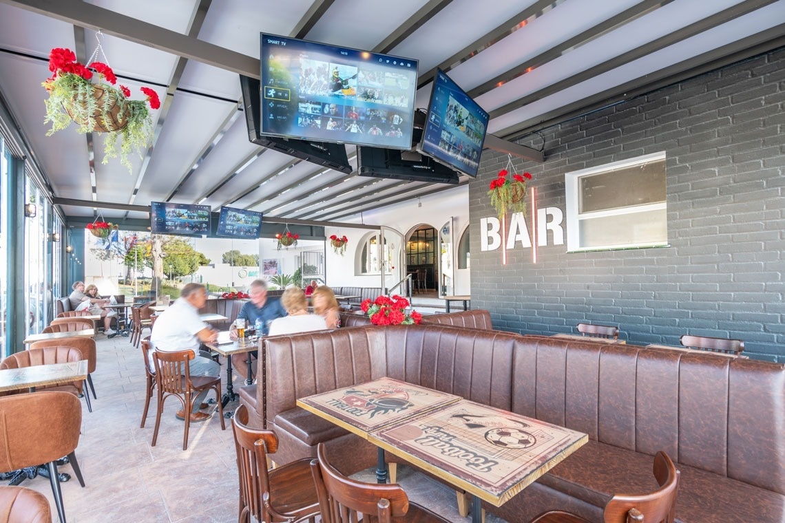 un grupo de personas se sienta en mesas en un restaurante con la palabra bar en la pared